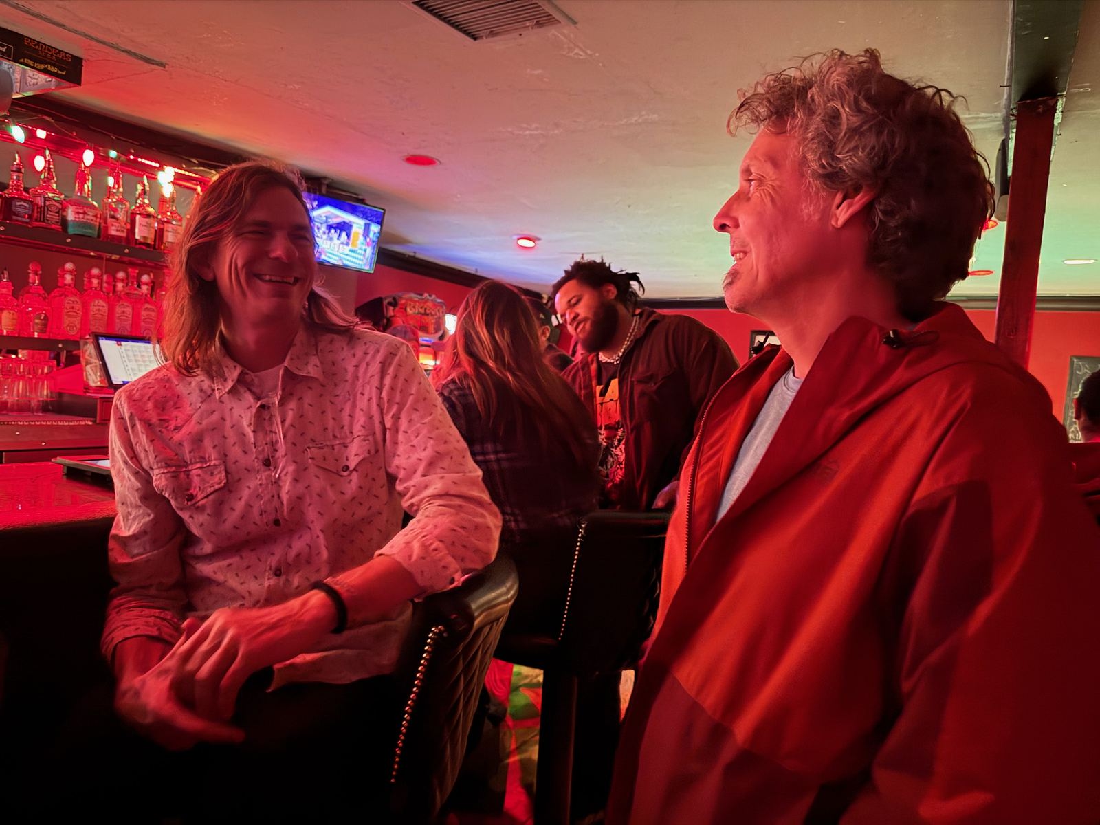 Alan and a friend laughing at a red neon-lit bar
