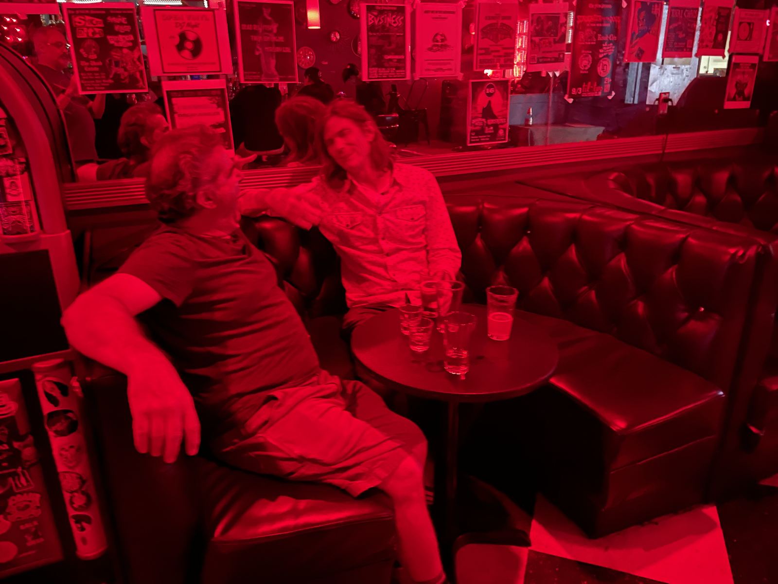 Alan and a friend in a red-lit dive bar booth with shot glasses
